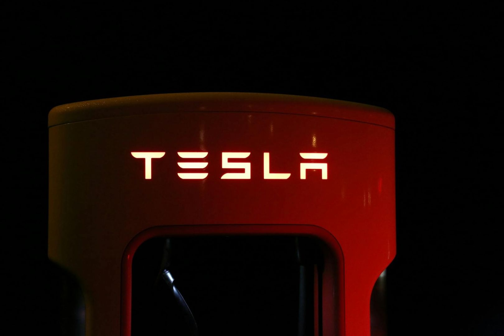Närbild av en röd Tesla Supercharger-laddstation i mörker.